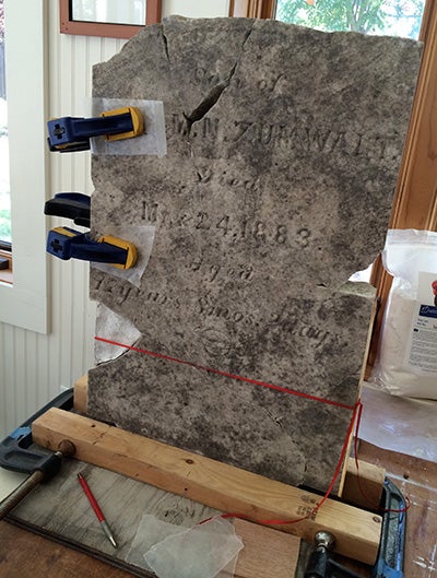 carefully placed clamps stabilize broken pieces of a gravestone 