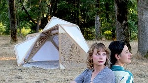 Photo of two women in a forest with an art installation in the background