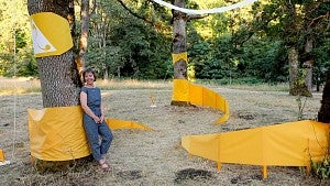 Photo of woman standing in trees with a bright yellow art installation 