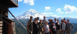 students stand next to fire lookout with Mt. Rainier in background
