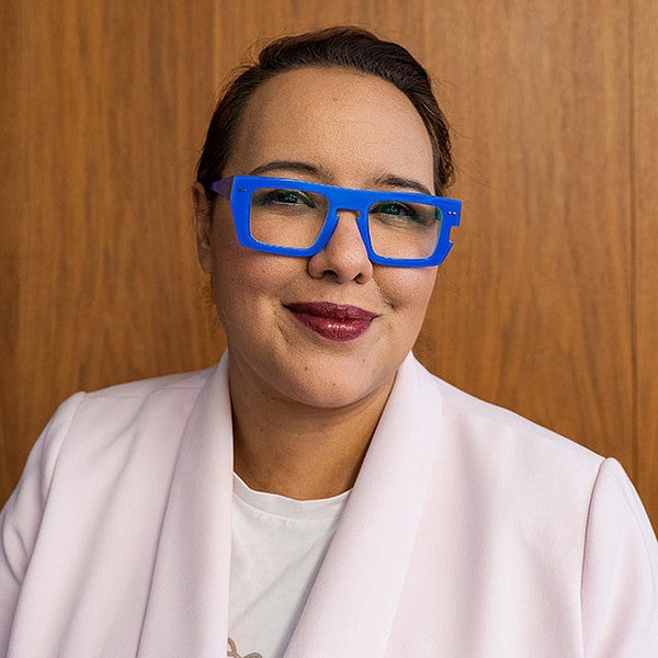 Portrait photo of Flavia Grey, PhD. Shows a smiling woman with chunky, bright blue glasses