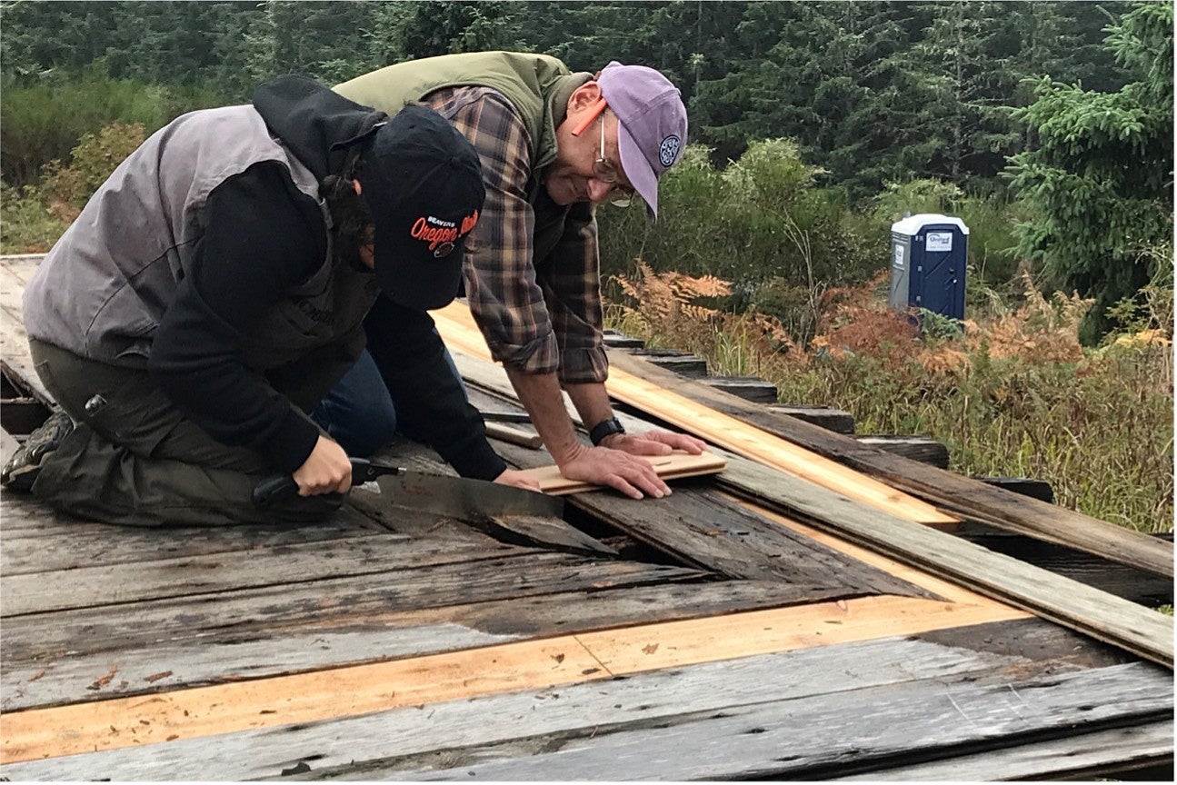 Close up detail photo of two individuals working to restore a wooden structure/deck. 