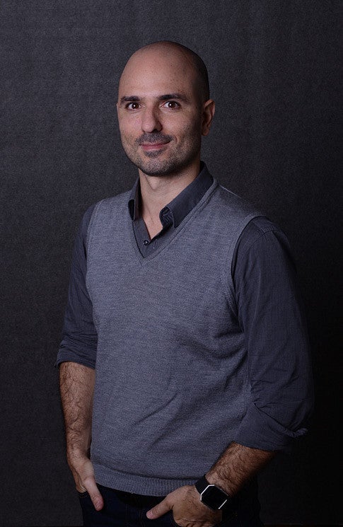 Ignacio Lopez Buson portrait photo. Image shows a smiling man in a vest and collared shirt on a dark gray background. 