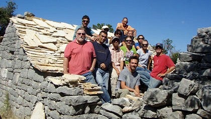 group stands inside stone house while working on roof at Croatia Field School