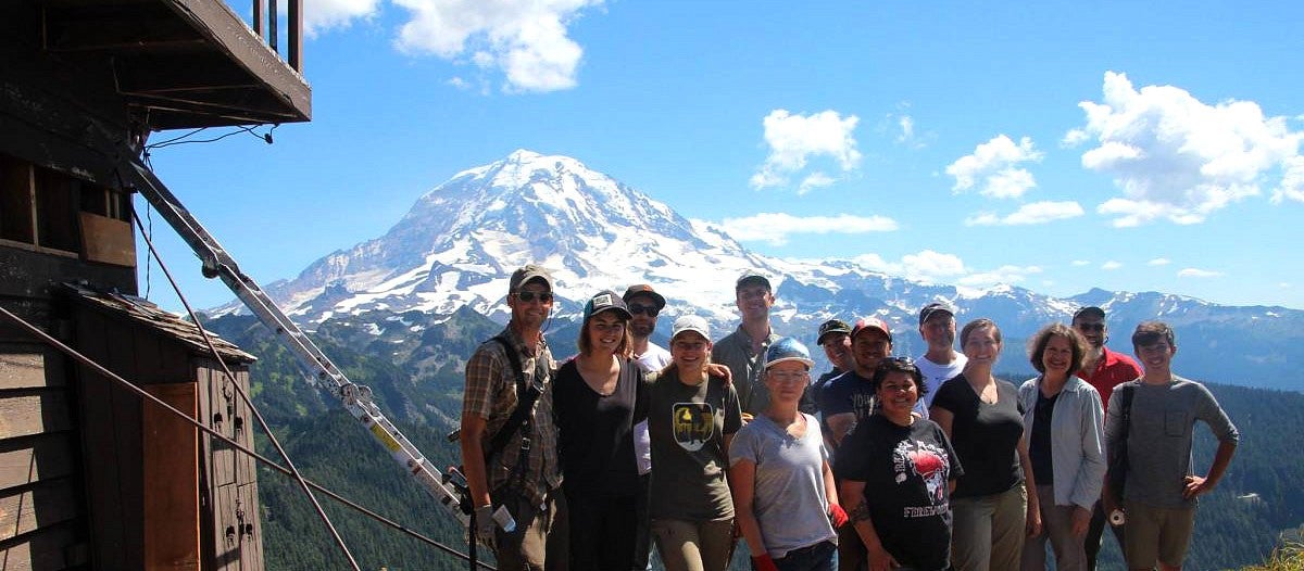 students stand next to fire lookout with Mt. Rainier in background