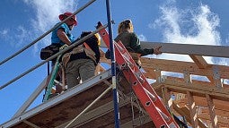 Photo of students working on house construction against a blue sky
