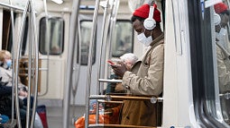 Man on a subway wearing a beanie, headphones, and a protective mask
