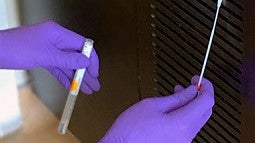 Gloved hands gathering a sample on a vent with a swab