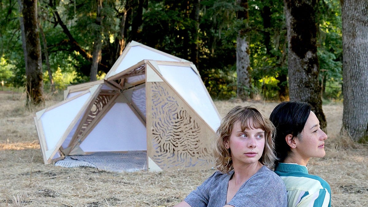 Photo of two women in a forest with an art installation in the background