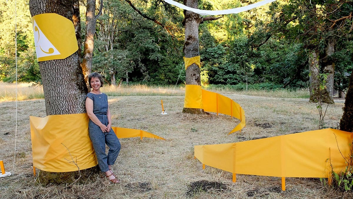 Photo of woman standing in trees with a bright yellow art installation 