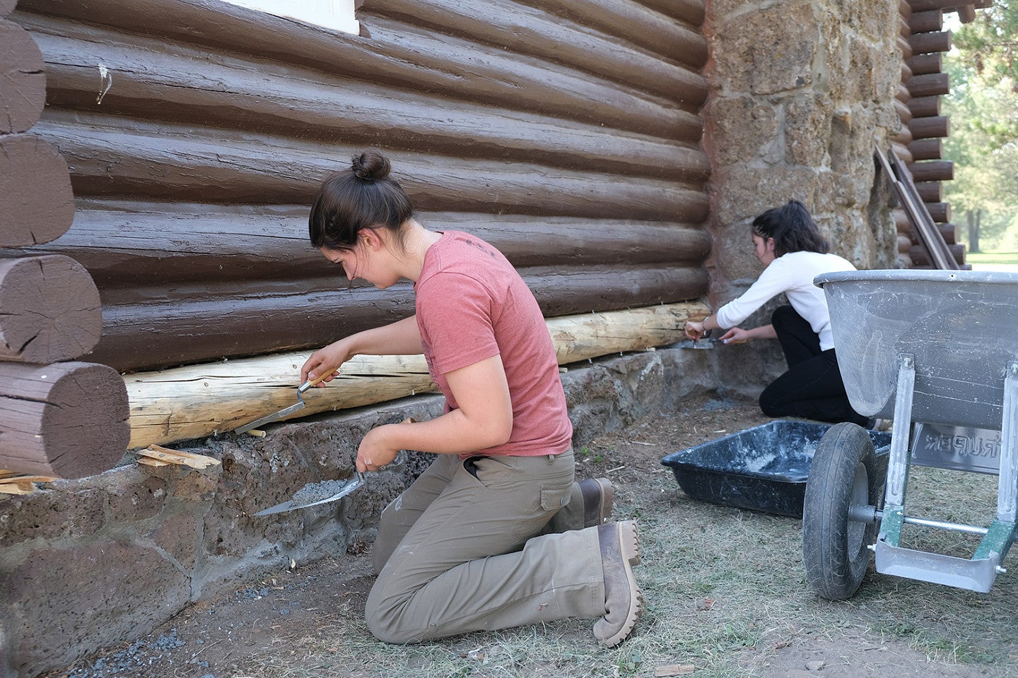 Photo from 2022 PNWPFS group shot of students working on a base log of a log cabin. 