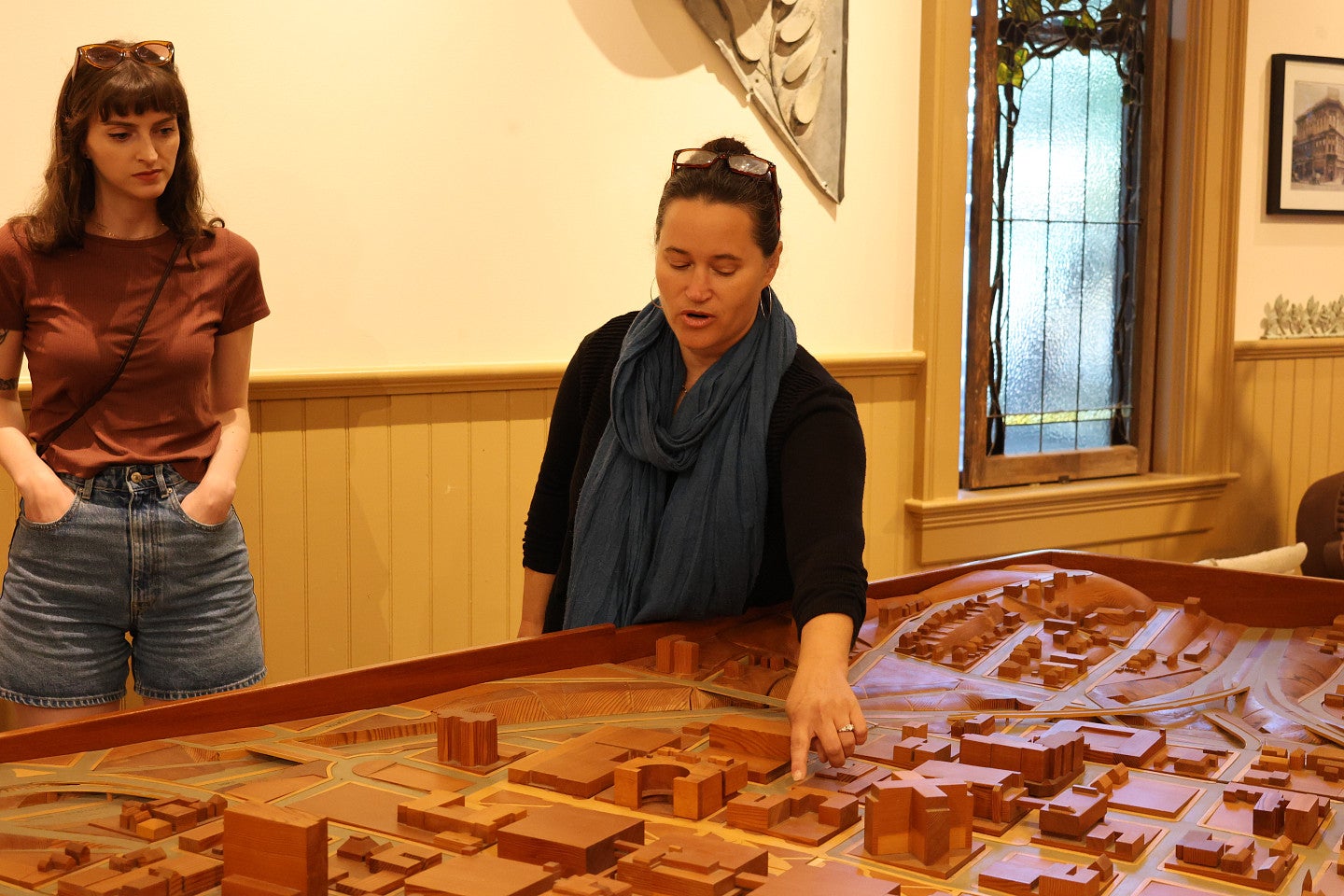 Photograph of an individual gesturing to points of interest on a carved, wooden map in Elk Rock Gardens while a student looks on. 