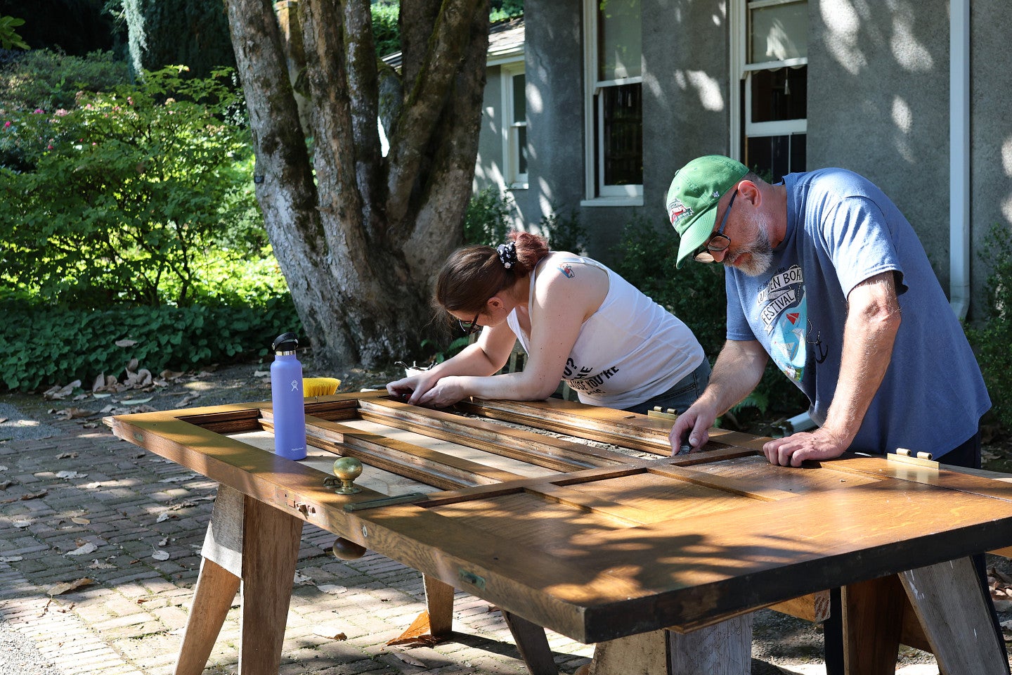 Preservationist and student work on wood door outside in Elk Rock gardens.