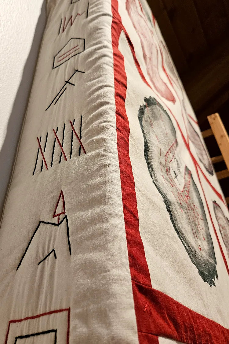 Close-up view of a piece of the exhibition. Shows a cloth covering a wood frame with symbols stitched into the fabric. 