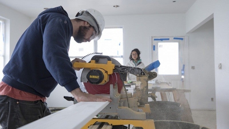 Student Eli Cox-Skall (right) cuts a baseboard while Ana Misenas prepares another baseboard for cutting.