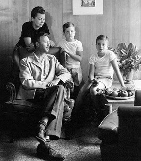 Photograph of the Belluschi family in a wood panelled room. Shows Pietro and his wife and two elementary age boys in a black and white photograph. 