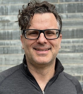 Uli Dangel's headshot. Shows a smiling man with glasses in front of a light brick wall.