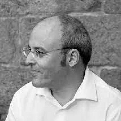 Photograph of a man in front of a brick wall. 